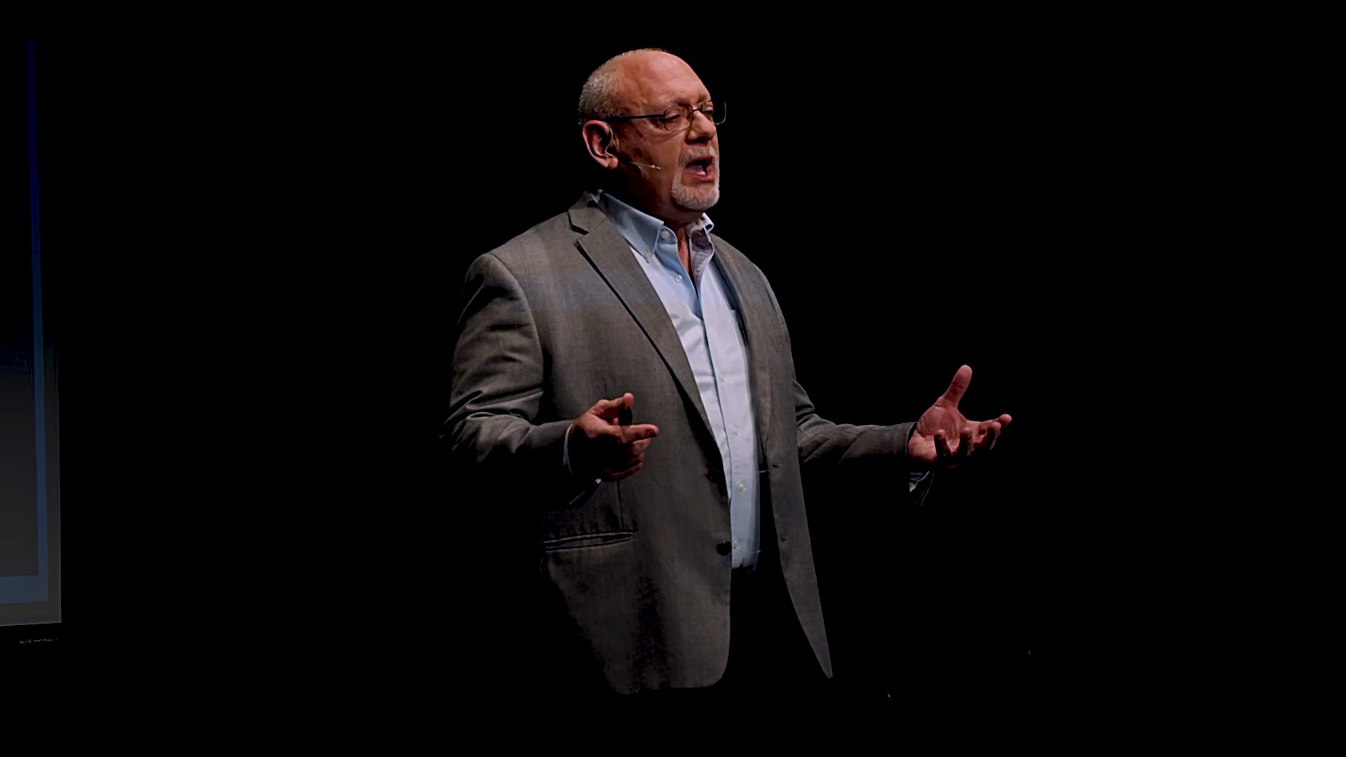 Bill Schuhlein on a dark stage with both arms open