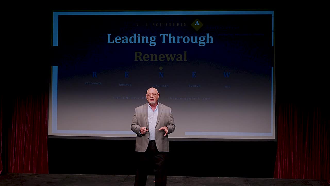 Bill Schuhlein on stage in front of a projected slide listing Recognize, Engage, Navigate, Evolve and Win